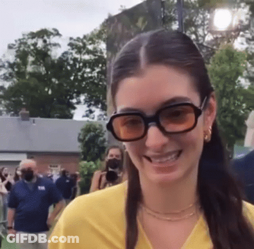 Woman In Sunglasses And Yellow Shirt Smiling Before Crowd GIF