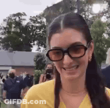 Woman In Sunglasses And Yellow Shirt Smiling In Front Of Crowd GIF