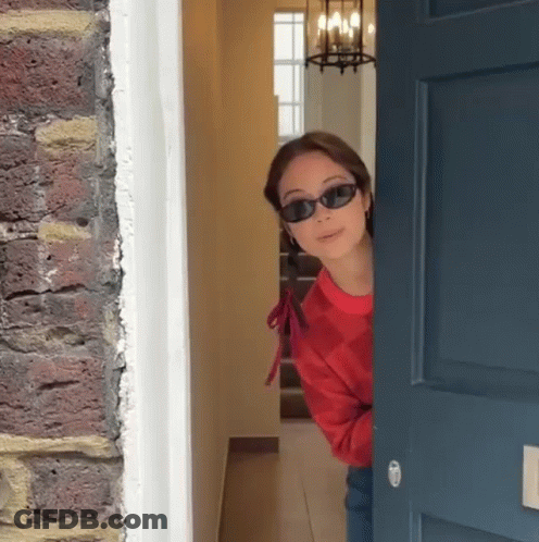 Woman In Sunglasses Peeking Out Door GIF