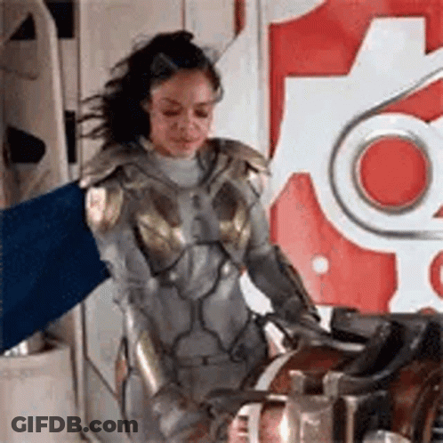 Woman In Superhero Costume Holding Blue Flag Next To Machine GIF