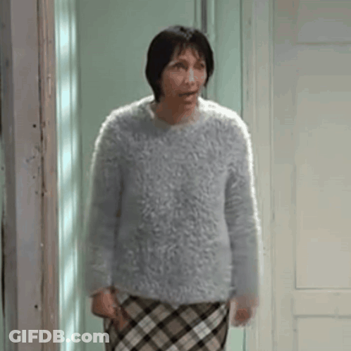Woman In Sweater And Plaid Skirt Standing In Front Of Door GIF