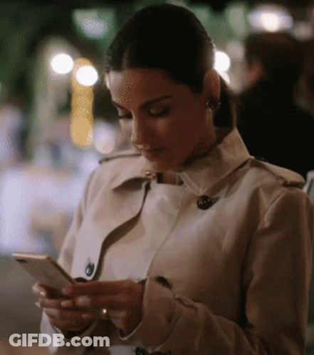 Woman In Trench Coat Looking At Phone GIF