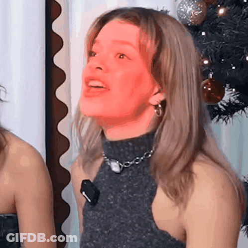 Woman In Turtleneck And Earrings Smiling With Christmas Tree GIF