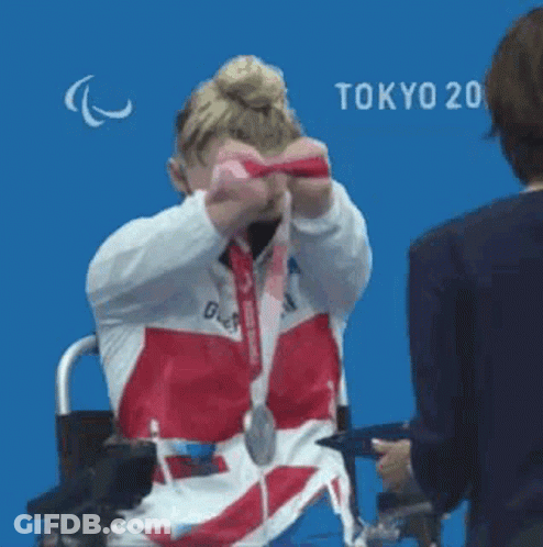 Woman In Wheelchair Holding Medal Against Blue Wall GIF