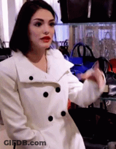 Woman In White Coat In Front Of Bags Display GIF