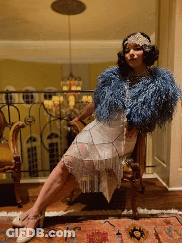 Woman In White Dress And Blue Feathered Jacket Sitting GIF