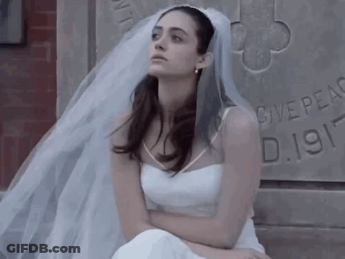 Woman In White Dress And Veil Sits By Stone Wall Saying Give Peace D.1911 GIF