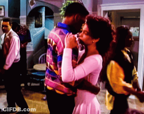 Woman In White Dress Hugging Man In Colorful Jacket GIF