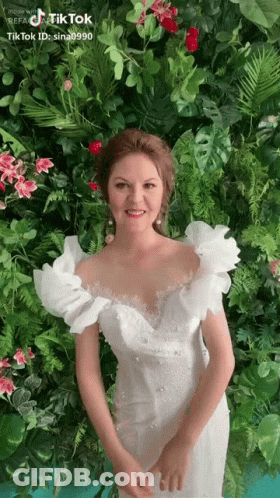 Woman In White Dress In Front Of Flower Wall GIF
