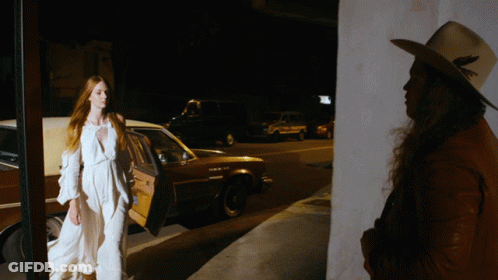 Woman In White Dress Next To Man In Hat GIF