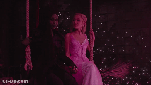 Woman In White Dress Next To Woman In Black Dress On Swing GIF