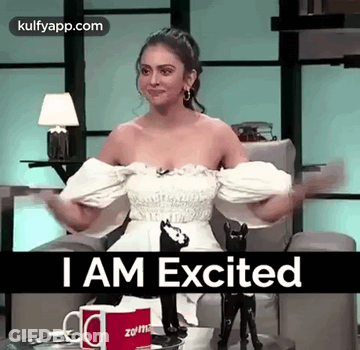 Woman In White Dress Sitting With Arms Outstretched Saying I Am Excited GIF