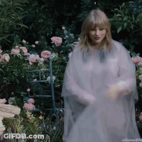 Woman In White Dress Standing In Garden With Pink Roses GIF