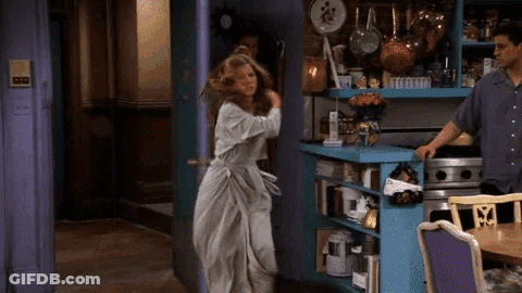 Woman In White Dress Standing In Kitchen With Man Behind Her GIF