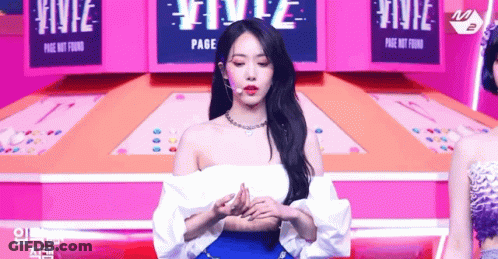 Woman In White Off-Shoulder Top And Blue Skirt On Stage With Microphone GIF