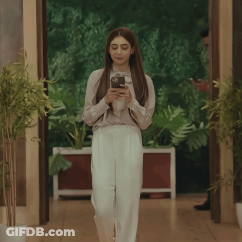 Woman In White Pants Looking At Phone While Walking GIF