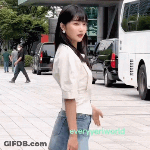 Woman In White Shirt And Blue Jeans Standing On Sidewalk GIF