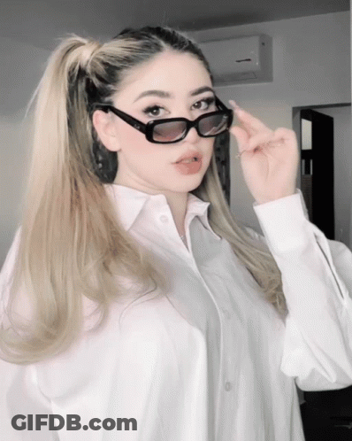 Woman In White Shirt And Sunglasses Looking At Camera GIF