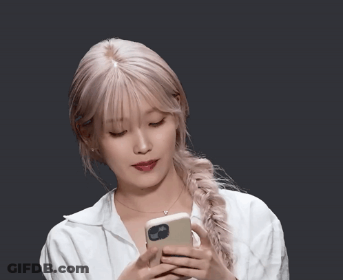 Woman In White Shirt Holding Phone With Braided Ponytail GIF