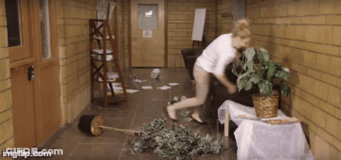 Woman In White Shirt Standing In Hallway With Potted Plant GIF