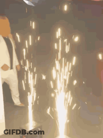 Woman In White Suit Next To Fireworks GIF