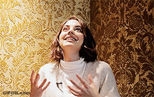 Woman In White Sweater In Front Of Gold Pattern Wall GIF