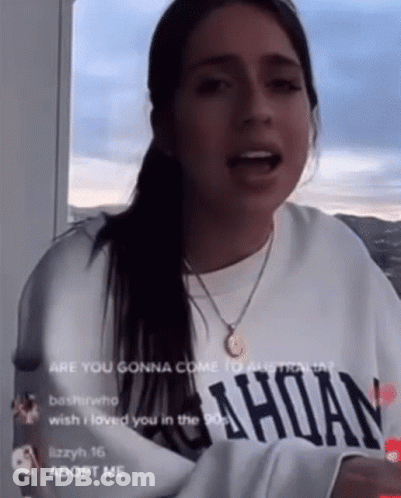 Woman In White Sweatshirt And Gold Necklace Talking On Balcony GIF