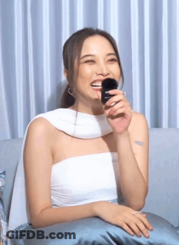 Woman In White Top Sitting On Couch Holding Brush In Mouth GIF
