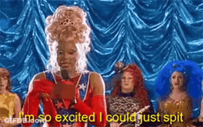 Woman In Wig Holding Microphone In Front Of Costumed Group GIF