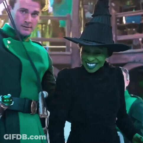 Woman In Witch Costume Smiling Next To Man In Green Coat GIF