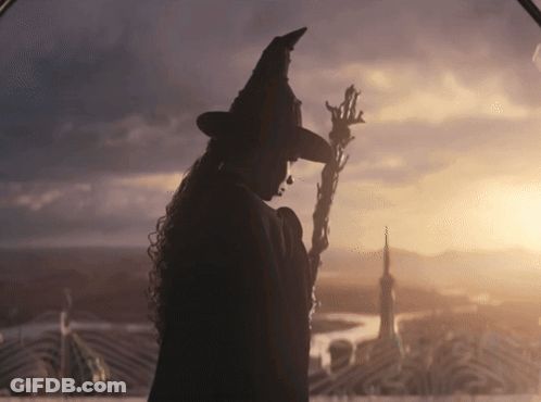 Woman In Witch Hat Holding Wand At Sunset GIF