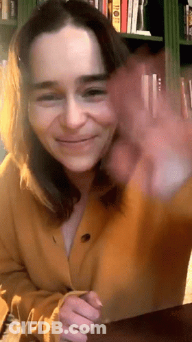Woman In Yellow Cardigan Smiling And Waving GIF