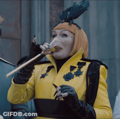 Woman In Yellow Coat And Black Gloves Drinking From Glass GIF