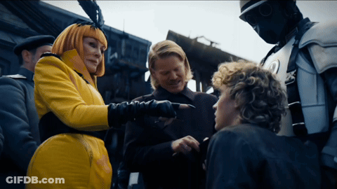 Woman In Yellow Coat Pointing At Man In Black Suit GIF
