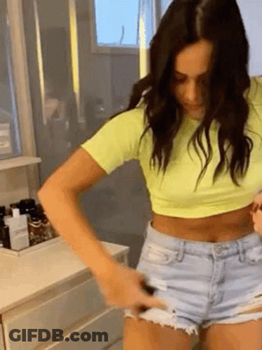 Woman In Yellow Crop Top And Denim Shorts In Bathroom GIF