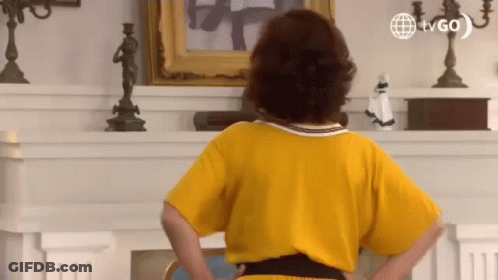Woman In Yellow Dress Hands On Hips By Fireplace GIF