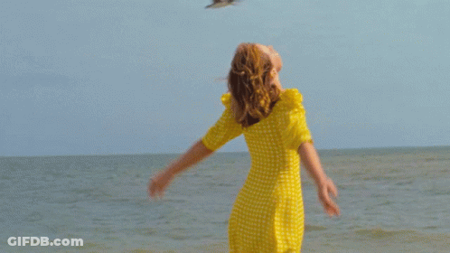 Woman In Yellow Dress With Arms Outstretched By Ocean GIF