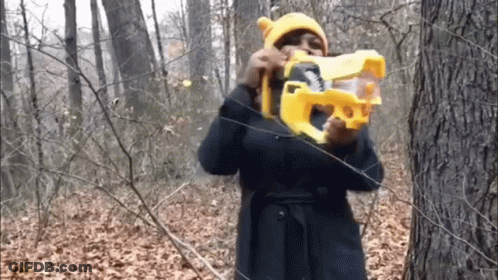 Woman In Yellow Hat Holding Toy Gun In Woods GIF