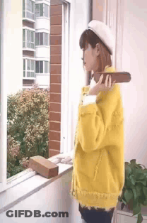 Woman In Yellow Jacket Holding Brick At Window GIF