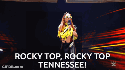 Woman In Yellow Jacket Holding Microphone Saying Rocky Top Tennessee GIF