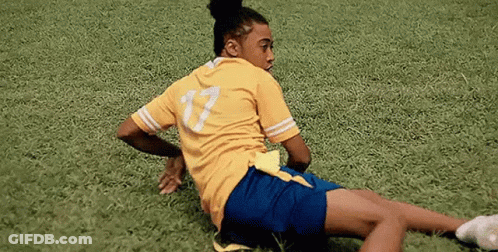 Woman In Yellow Shirt And Blue Shorts Laying On Soccer Field GIF