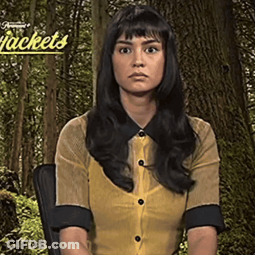 Woman In Yellow Shirt Sitting In Front Of Jackets Sign GIF