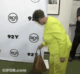 Woman In Yellow Suit Holding Brown Purse GIF