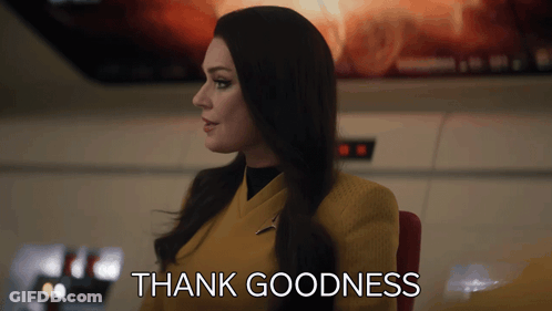Woman In Yellow Suit Sitting In Front Of Thank Goodness Sign GIF