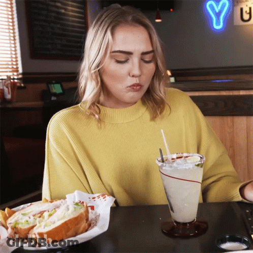 Woman In Yellow Sweater With Sandwich And Drink GIF