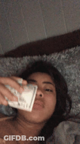Woman Laying On Bed Holding Money In Mouth GIF