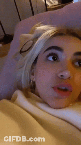 Woman Laying On Bed In Glasses And White Sweater GIF