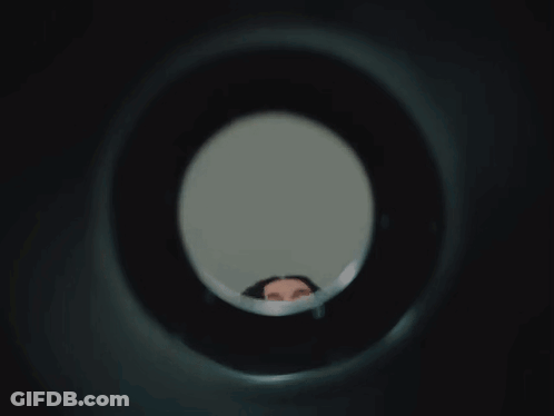 Woman Looking Through Hole In Wall GIF