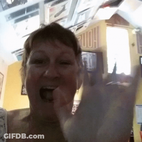 Woman Making Horns Sign In Front Of Home Sign GIF