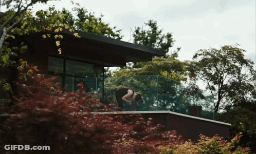 Woman On Balcony In Front Of House Surrounded By Trees GIF